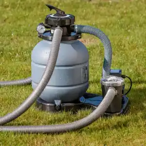 Pool filtration system on a lawn: round gray sand filter with hoses connected to a pump and valve.