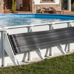 Above-ground pool with a black solar cover rolled on a white frame, near a stone-clad house with arches and lounge chairs on the patio.