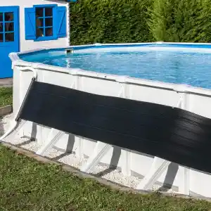 Above-ground pool with a black safety cover partially rolled across the side, white frame, blue water, and a blue-shuttered shed behind a green hedge.