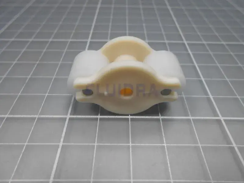 clorador-salino-gre-swc-conectado-todo-en-uno-ph-2 | PisciManía Small cream-colored plastic clamp/bearing holder with two entering holes and a central circular boss, resting on a gray grid cutting mat.
