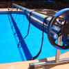 Manual pool-cleaning reel with hose laid along the edge of a blue swimming pool.